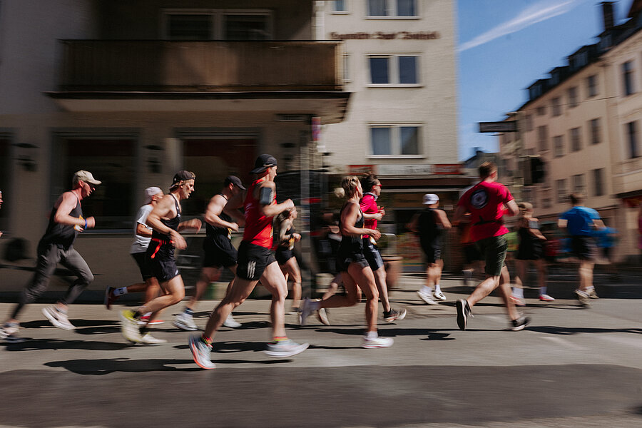 Menschen in Sportkleidung laufen über eine Straße bei einem Stadtlauf.