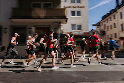 Menschen in Sportkleidung laufen über eine Straße bei einem Stadtlauf.